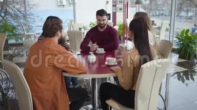 一群白人年轻人在餐馆聊天的中镜头。 坐在餐桌前的男女朋友